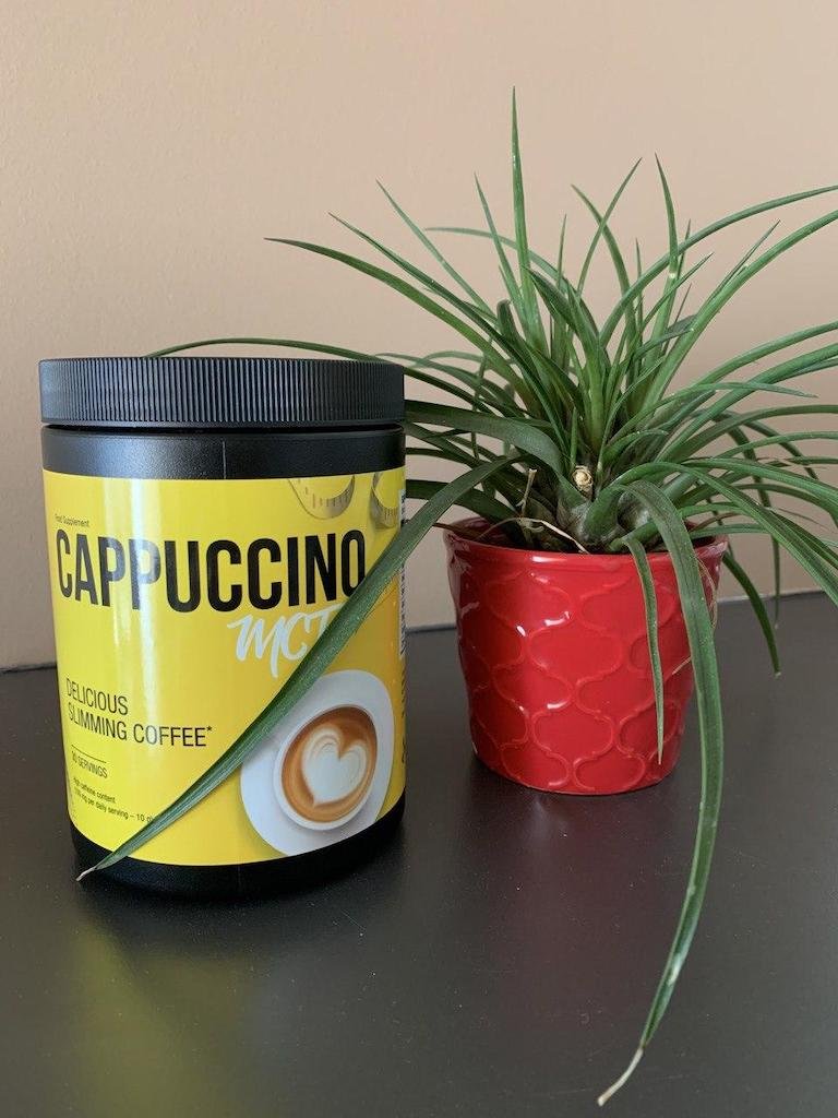 envase de cappuccino MCT de color amarillo y letras negras junto a planta ornamental.