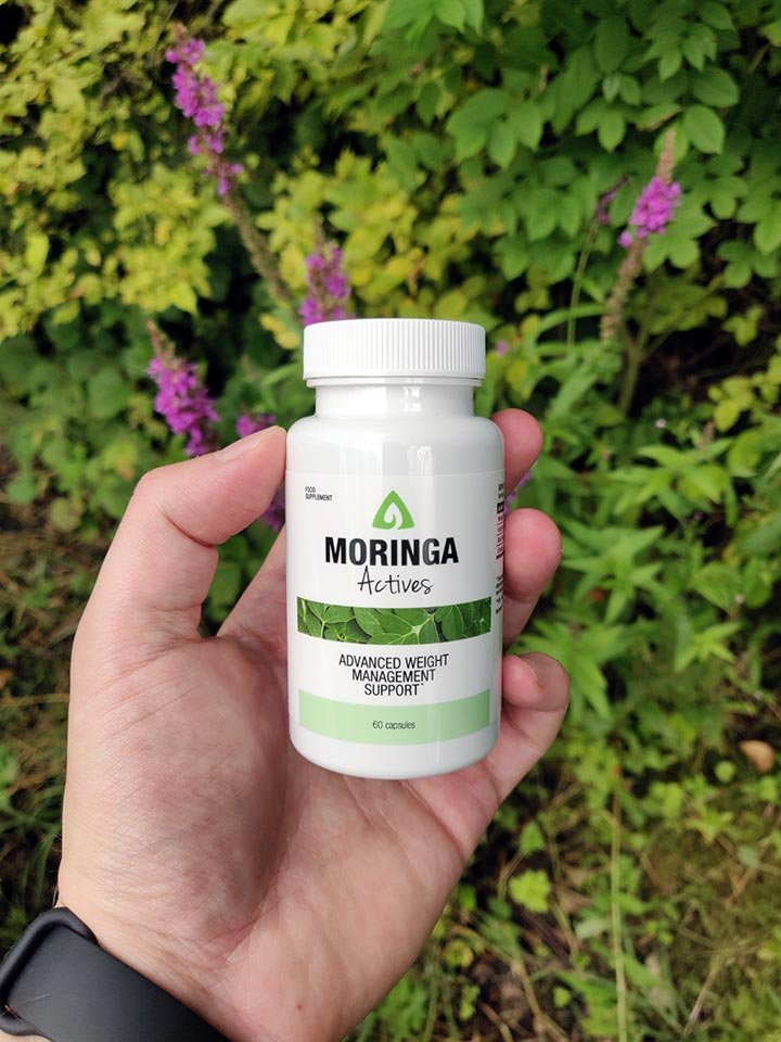 envase blanca y verde con letras negras sostenido en una mano en la naturaleza.