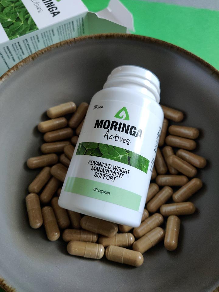 caja con envase blanca y verde con letras negras dentro de cuenco con capsulas de suplemento