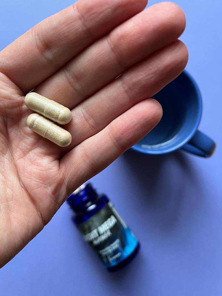 envase de suplemento de colores negros y azul con letras blancas capsulas en la mano.