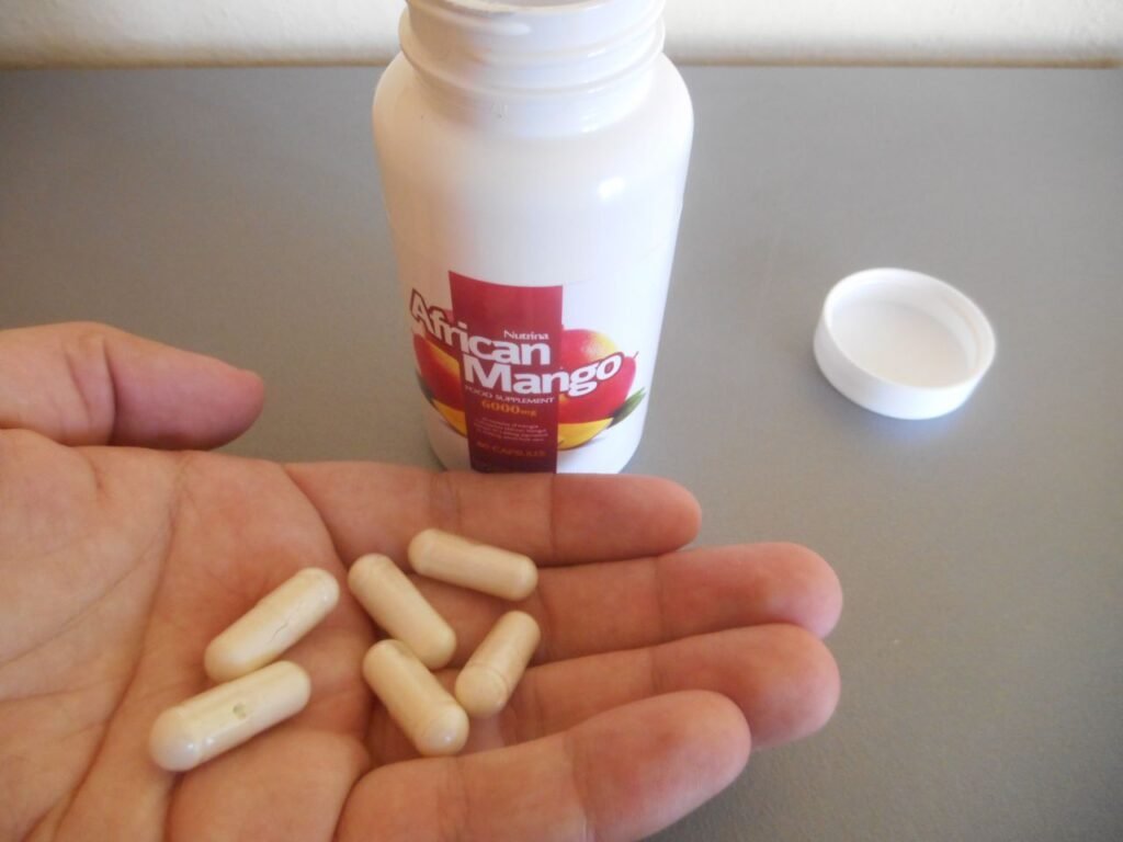 mano con pastillas de suplemento, bote de pastillas de color blanco con imagen de mango y letras blancas