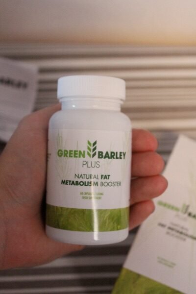 envase de green barley plus con fondo blanco y naturaleza verde con letras verdes sostenido por una mano.