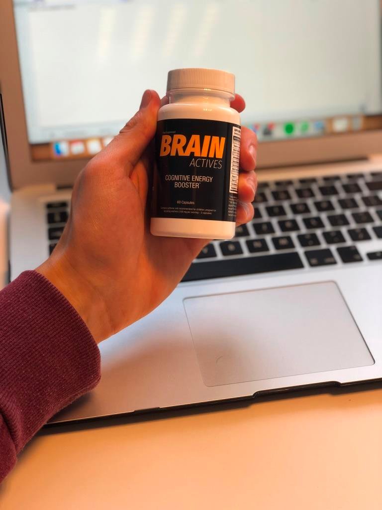 mano sosteniendo bote de suplemento junto a ordenador portátil