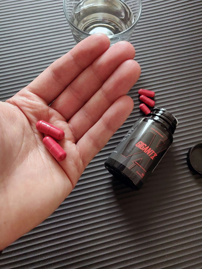 Bote de suplemento negra con letras rojas, capsulas de suplemento en una mano.