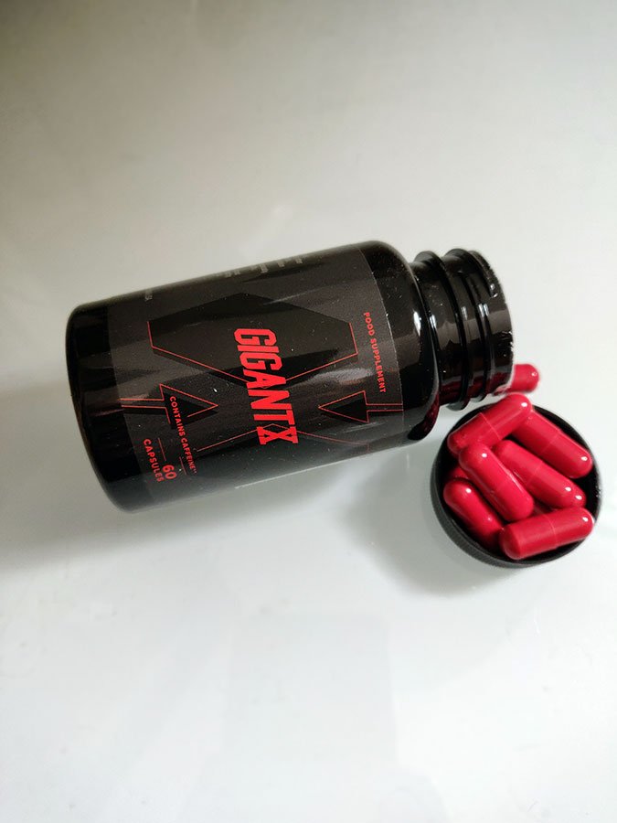 Bote de suplemento negra con letras rojas, cápsulas en la tapa
