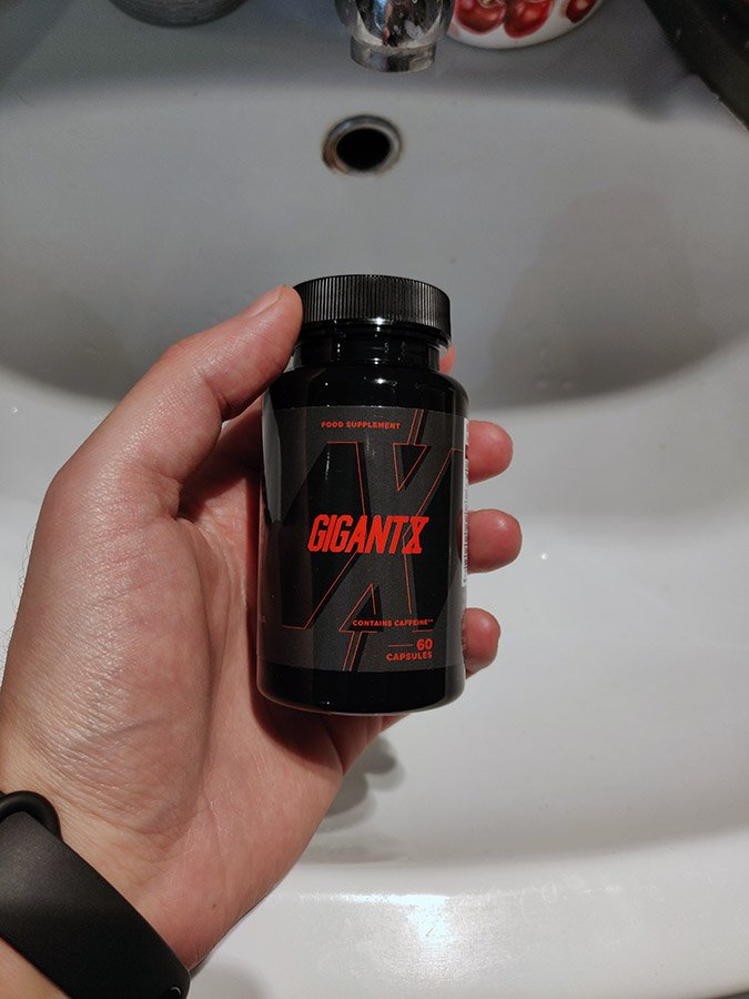 Bote de suplemento negra con letras rojas sostenidas por una mano.