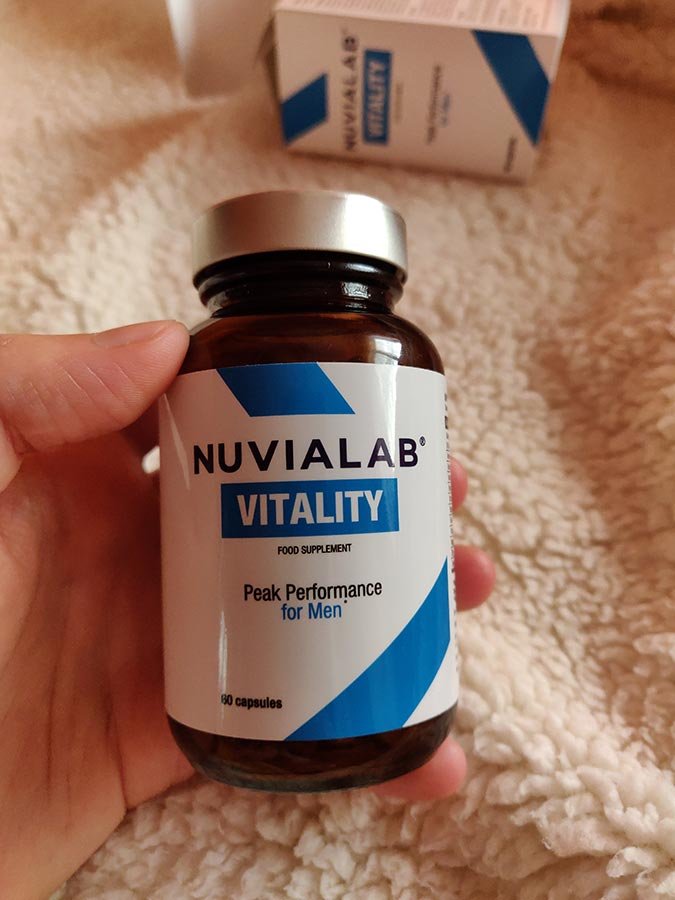 Bote de suplemento blanca con letras negras y azules, sujeto por una mano.